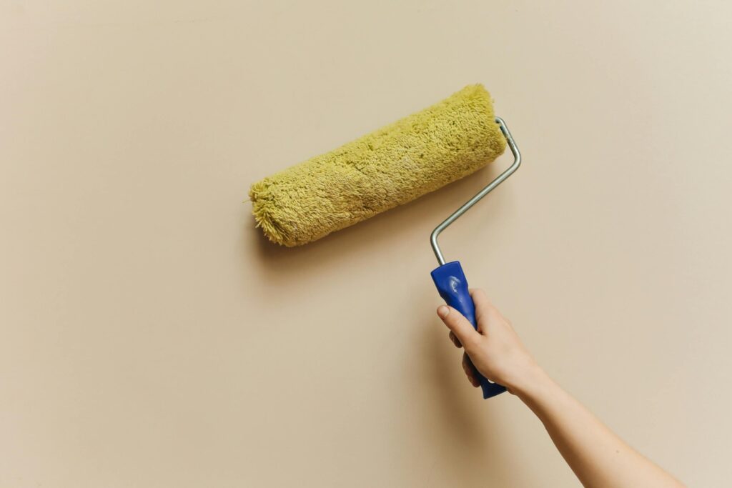 pexels-photo-5583126-5583126 A hand using a yellow paint roller to paint a beige wall. Perfect for DIY and home improvement themes.