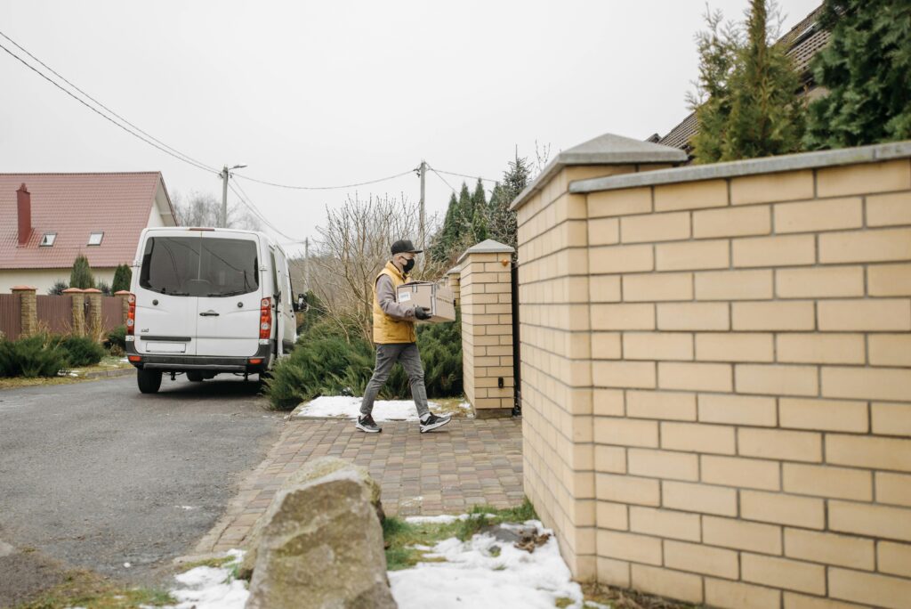 Courier delivers a package in suburban neighborhood with white delivery van nearby.